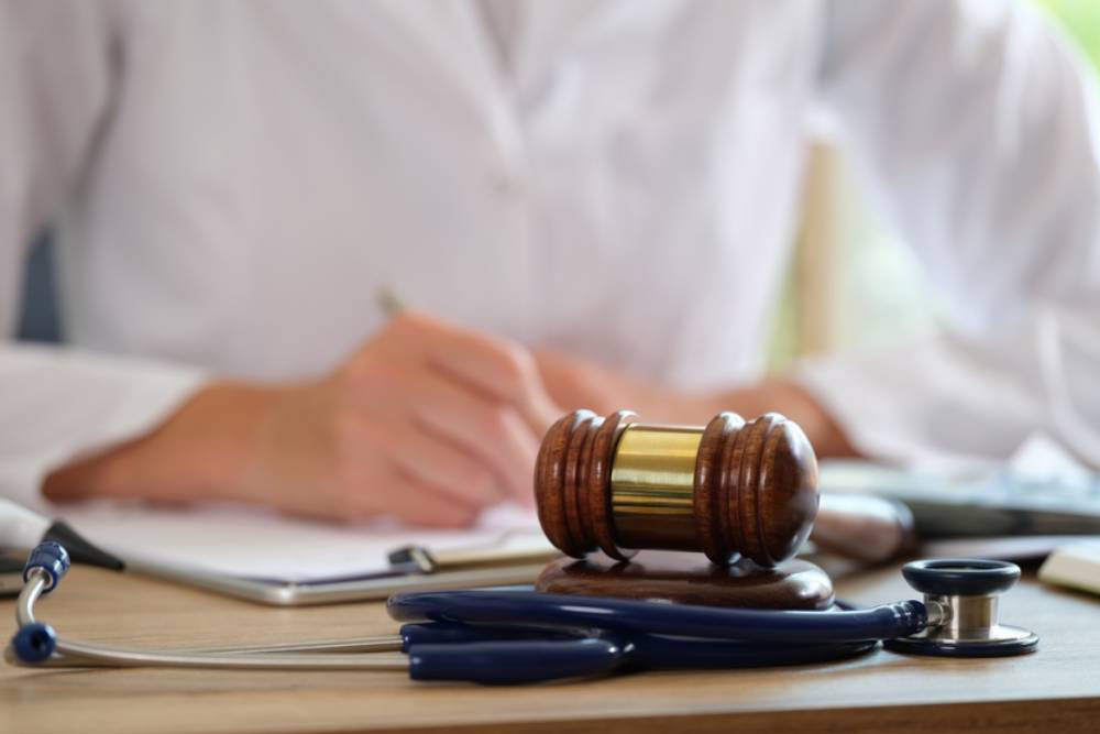Court gavel with stethoscope on a table in background doctor writes notes.