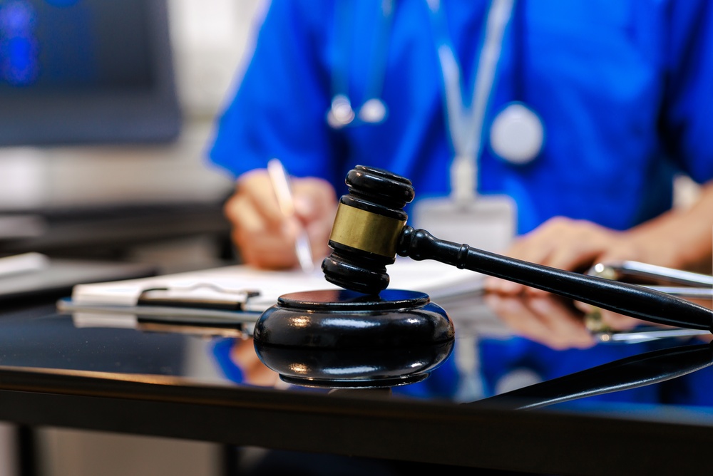  judge gavel on desk with blurred healthcare professional in blue scrubs writing in background, concept of medical law, malpractice, insurance, compliance, court